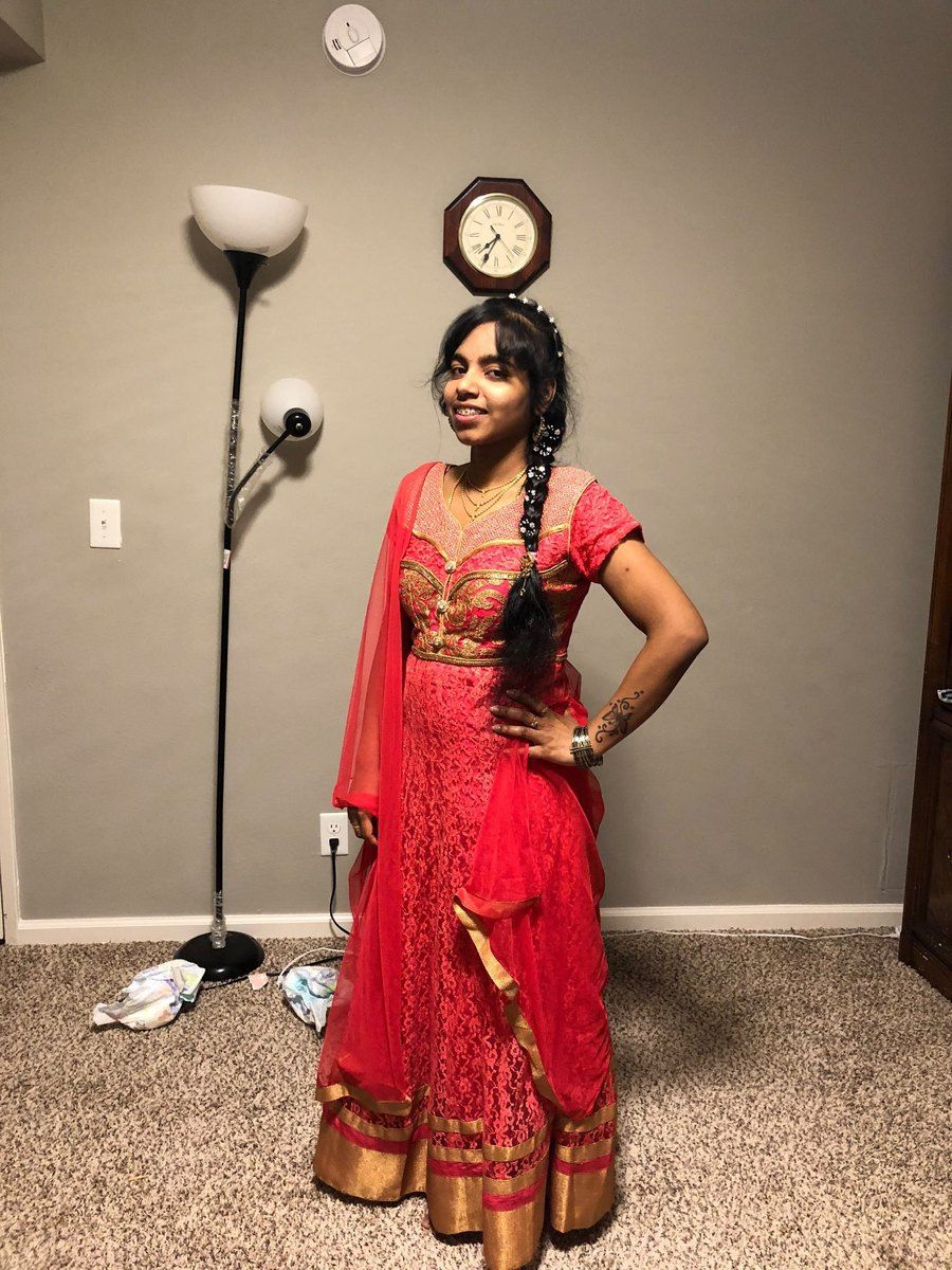 Nithya further along her transformation, in the same coral-pink dress with her hair in a long braid, at home